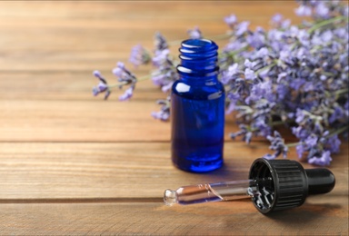 Photo of Bottle of essential oil and lavender flowers on wooden background. Space for text