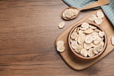 Photo of Bowl and spoon with dried banana slices on wooden table, flat lay. Space for text