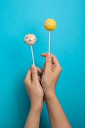 Woman holding bright delicious cake pops on color background, closeup