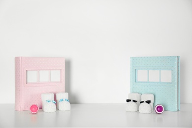 Photo of Photo albums with bootees and rattles for baby room interior on table near white wall