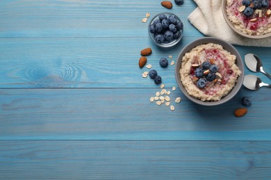 Photo of Tasty oatmeal porridge with toppings on light blue wooden table, flat lay. Space for text
