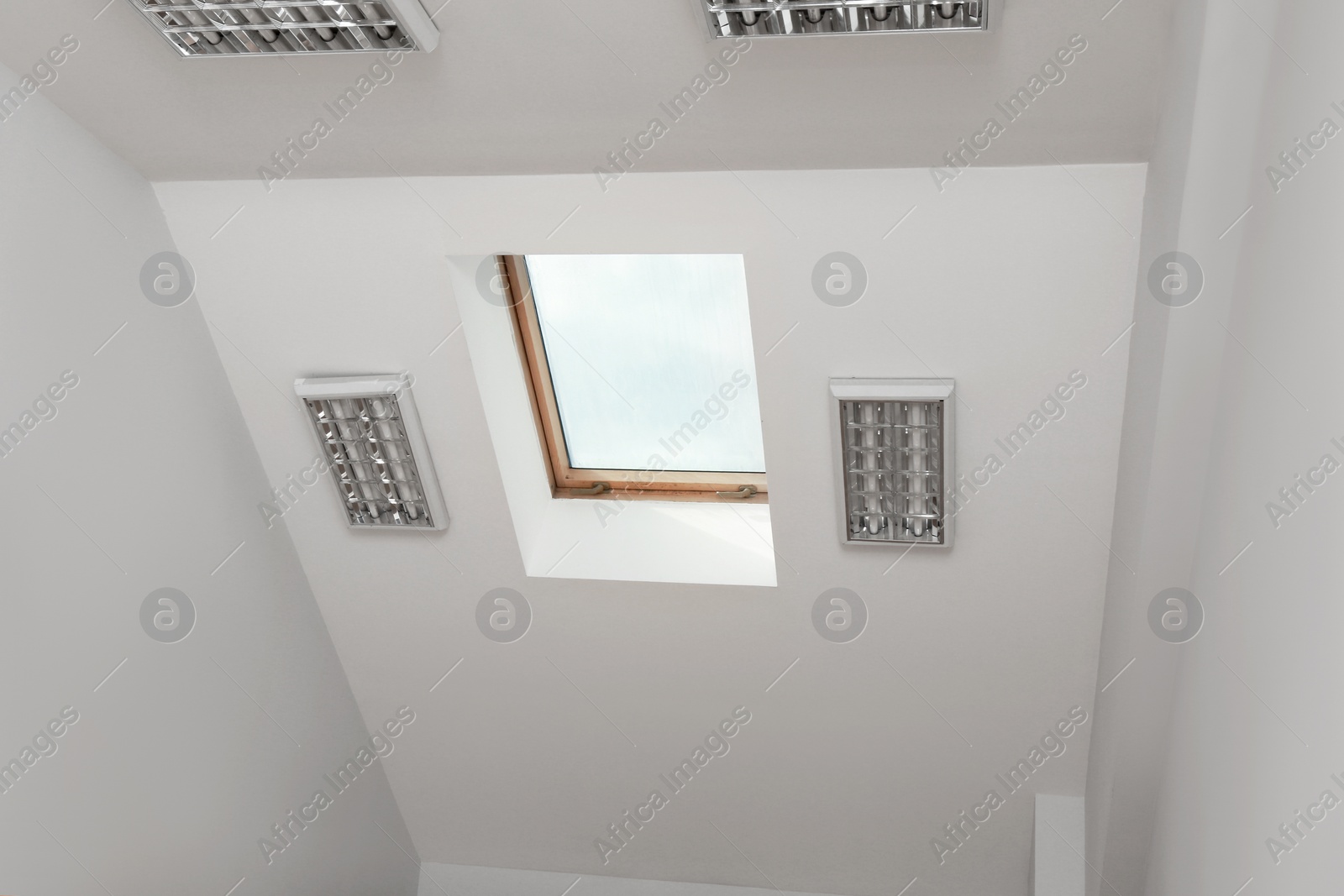 Photo of Skylight roof window and lamps on slanted ceiling in attic room, low angle view