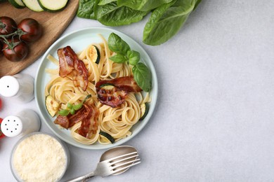 Photo of Tasty pasta with bacon and basil on light grey table, flat lay. Space for text