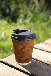 Takeaway cardboard coffee cup with plastic lid on wooden table outdoors