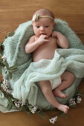 Photo of Adorable little baby with green blanket and floral decor on wooden background, top view