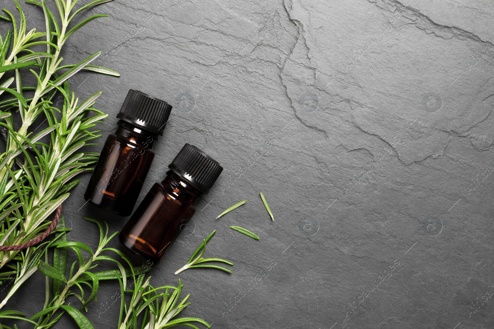 Photo of Bottle of essential oil and fresh rosemary on black table, flat lay. Space for text