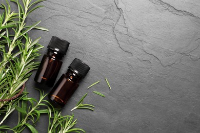Photo of Bottle of essential oil and fresh rosemary on black table, flat lay. Space for text