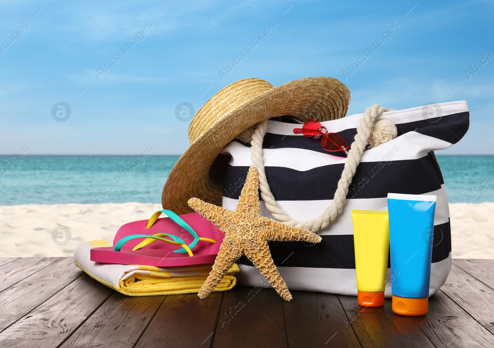 Image of Stylish bag with beach accessories on wooden surface near seashore