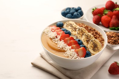 Photo of Delicious smoothie bowl with fresh berries, banana, coconut flakes and granola on white table. Space for text