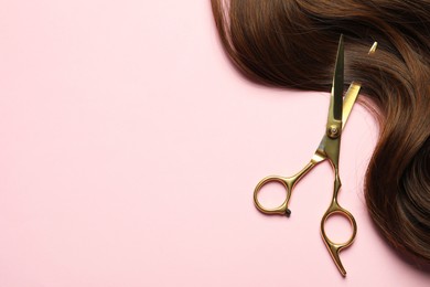 Photo of Professional hairdresser scissors with brown hair strand on pink background, top view. Space for text