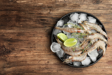 Photo of Fresh raw shrimps with ice on wooden table, top view. Space for text