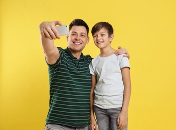 Dad and his son taking selfie on color background