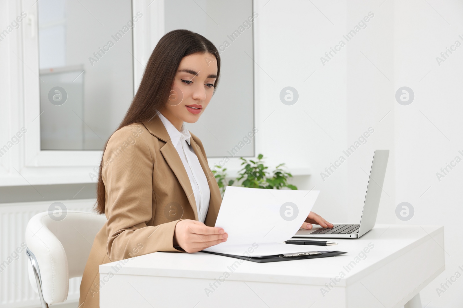 Photo of Young female intern working with laptop at table in office