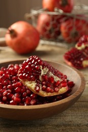 Photo of Ripe juicy pomegranate grains in bowl on wooden table, closeup