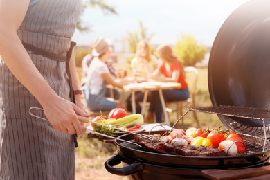 Image of Man cooking meat and vegetables on barbecue grill outdoors, closeup
