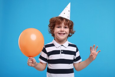 Photo of Happy little boy in party hat with balloon on light blue background
