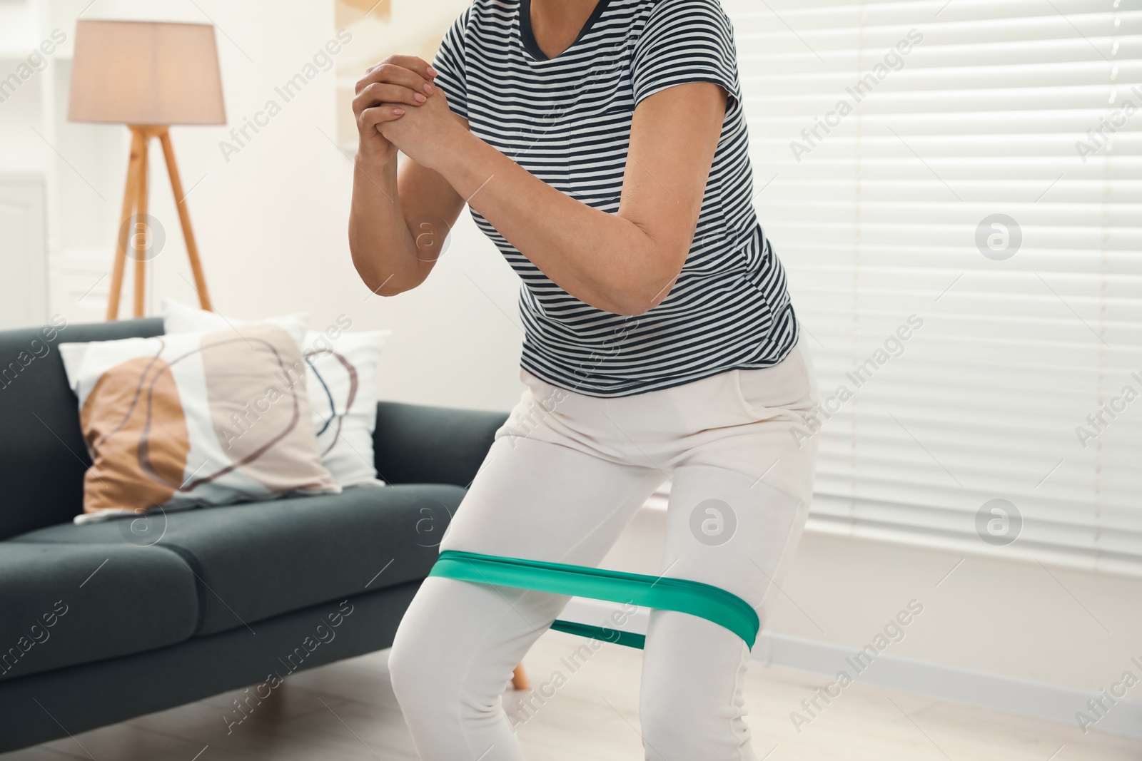 Photo of Senior woman doing squats with fitness elastic band at home, closeup