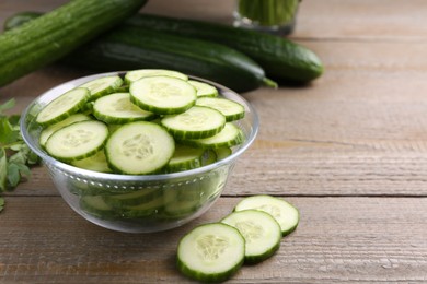 Photo of Cut cucumber in glass bowl and fresh vegetables on wooden table, closeup. Space for text