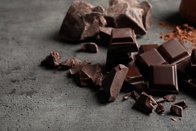 Pieces of chocolate and cocoa powder on grey background