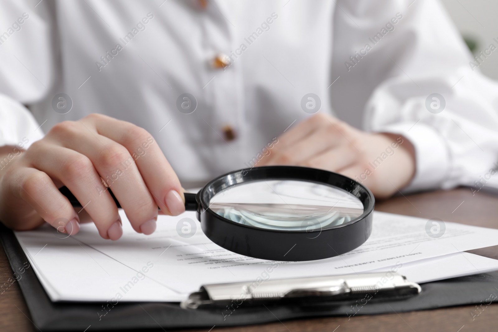 Photo of Woman looking at document through magnifier at wooden table, closeup. Searching concept