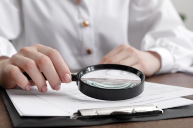 Photo of Woman looking at document through magnifier at wooden table, closeup. Searching concept