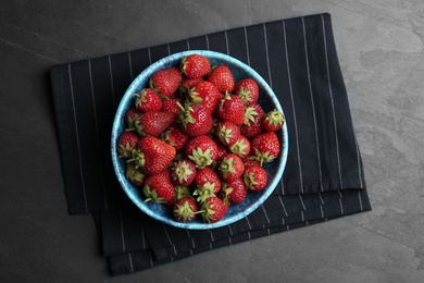 Photo of Delicious ripe strawberries in bowl on black table, flat lay