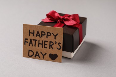Card with phrase HAPPY FATHER'S DAY and gift box on light grey background