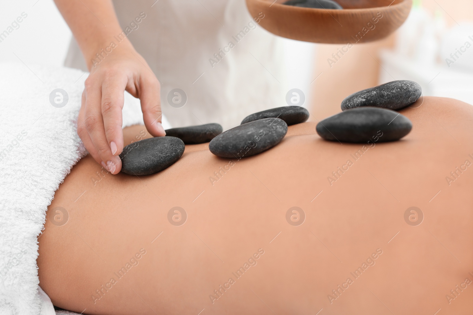 Photo of Beautiful young woman getting hot stone massage in spa salon