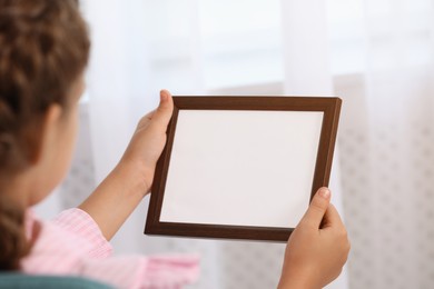 Photo of Little girl holding empty photo frame indoors, closeup
