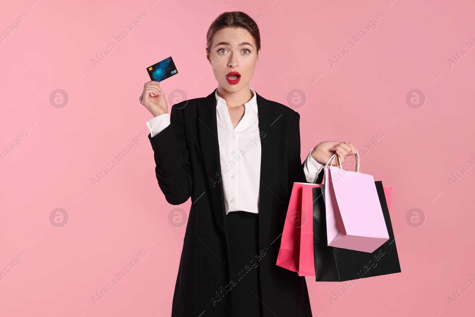 Photo of Surprised young woman with shopping bags and credit card on light pink background. Big sale