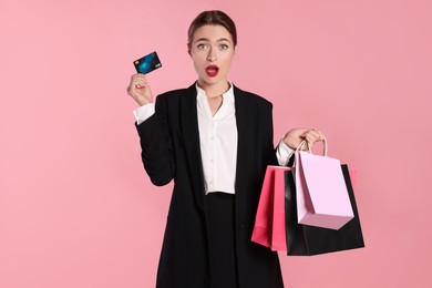 Photo of Surprised young woman with shopping bags and credit card on light pink background. Big sale