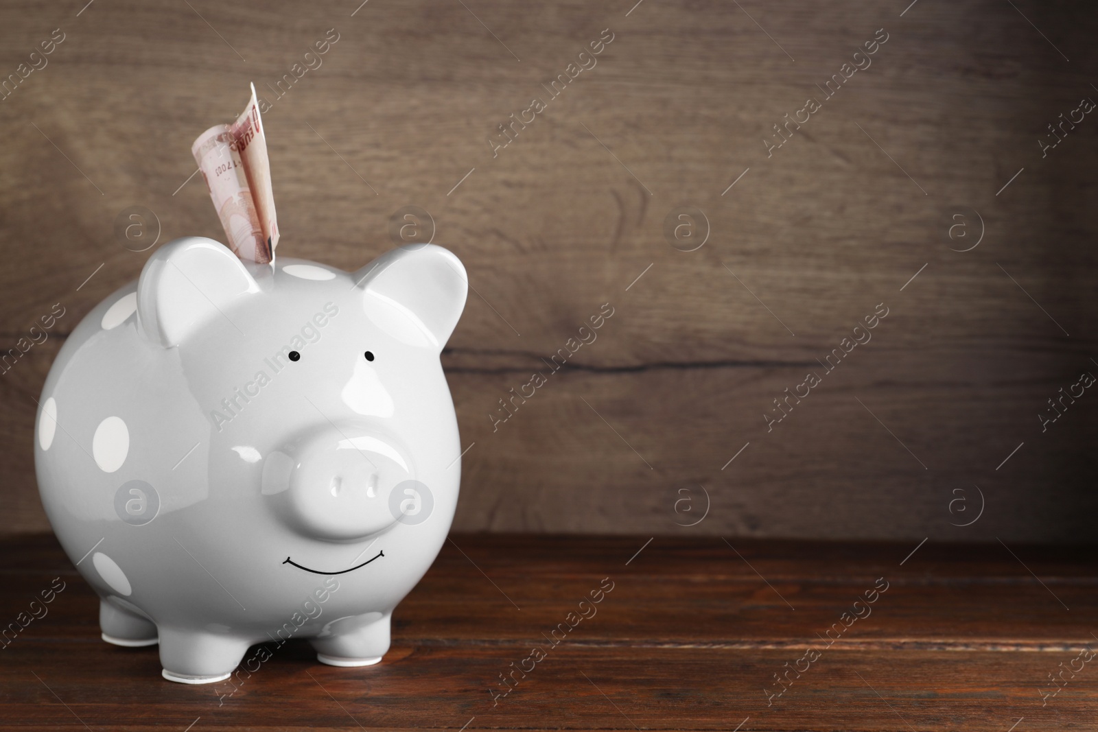 Image of Grey piggy bank with money on wooden table, space for text