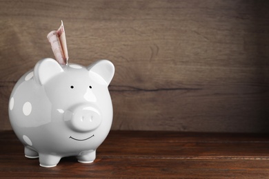 Grey piggy bank with money on wooden table, space for text