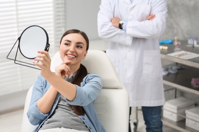 Young woman looking at her new dental implants in mirror indoors