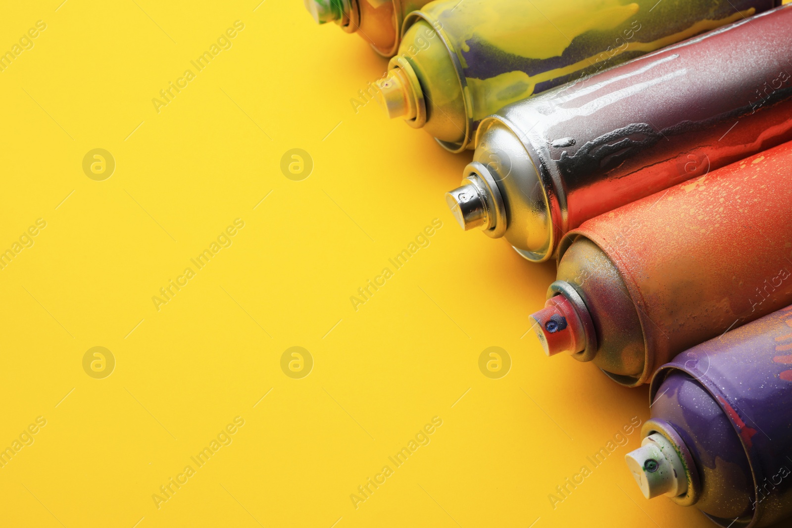 Photo of Used cans of spray paints on yellow background, space for text. Graffiti supplies