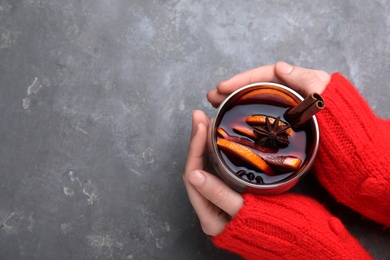 Photo of Woman with glass of mulled wine at grey table, top view. Space for text