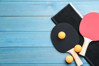 Photo of Ping pong rackets, net and balls on light blue wooden table, flat lay. Space for text