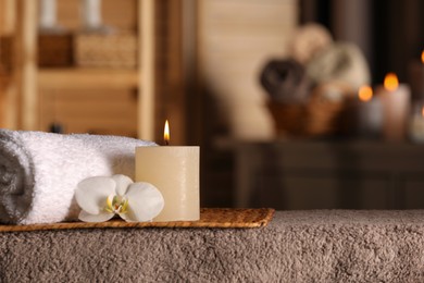 Photo of Spa composition with candle, orchid flower and rolled towel on massage table in wellness center, space for text