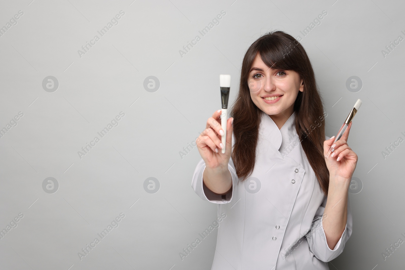 Photo of Cosmetologist with cosmetic brushes on grey background, space for text