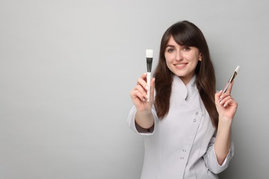 Cosmetologist with cosmetic brushes on grey background, space for text