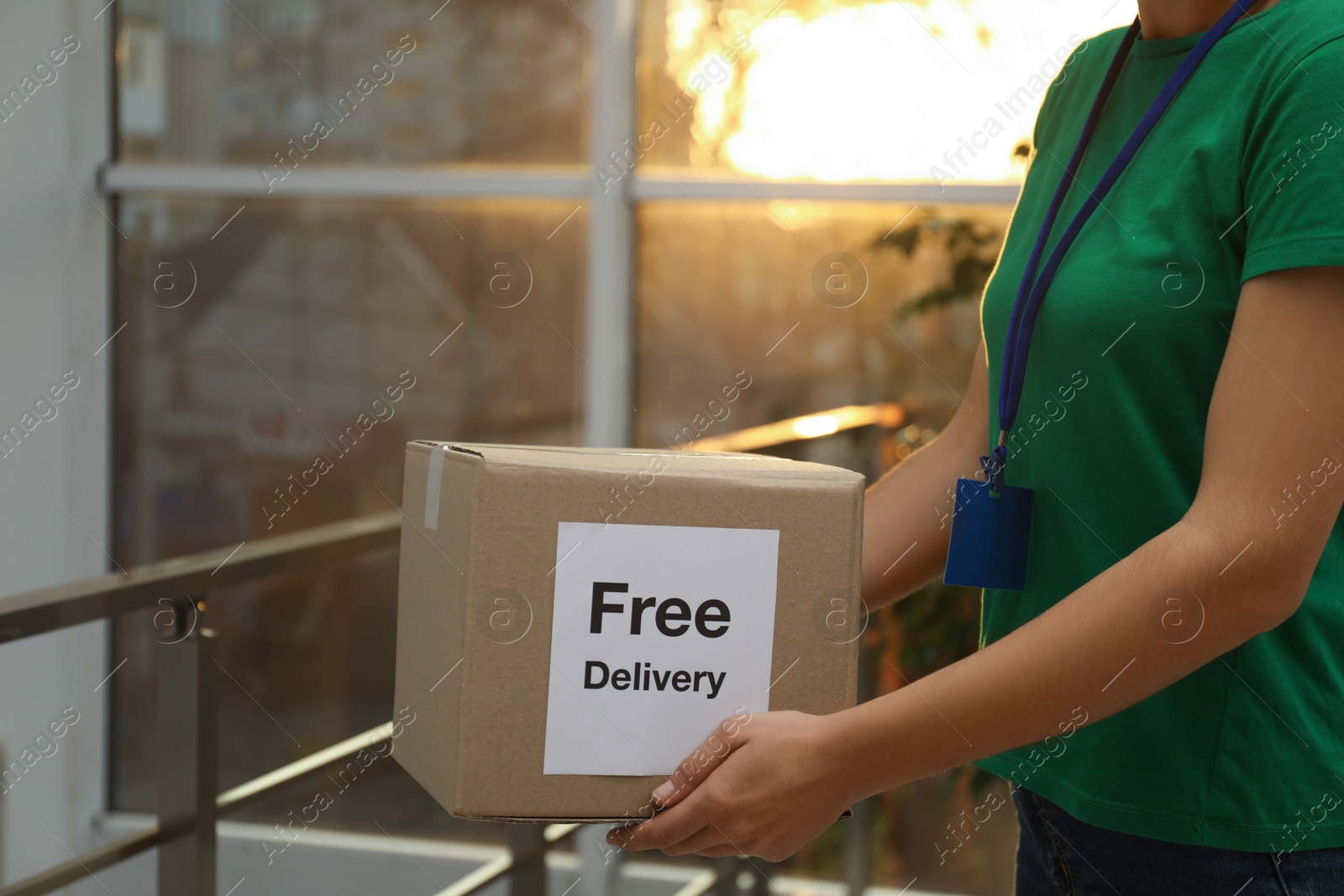 Photo of Courier holding parcel with sticker Free Delivery indoors, closeup