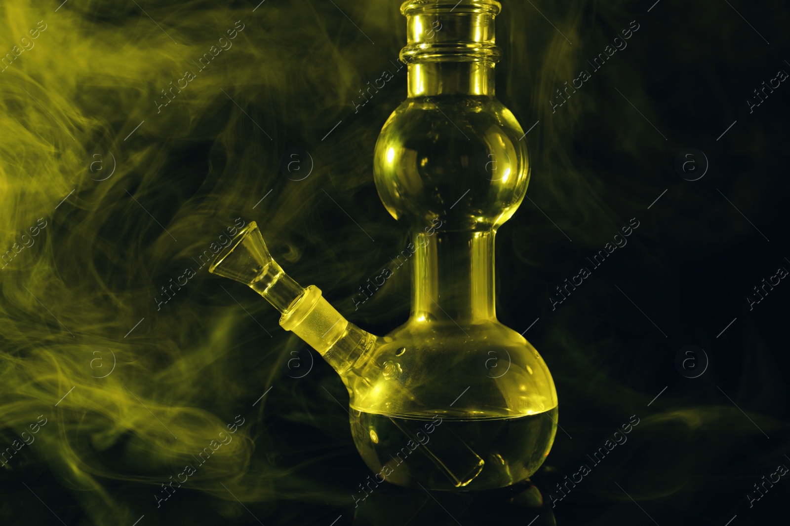Photo of Glass bong and smoke on black background, toned in yellow. Smoking device