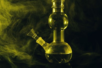 Glass bong and smoke on black background, toned in yellow. Smoking device