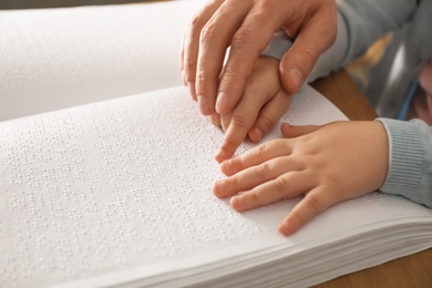 Man teaching child to read book written in Braille, closeup