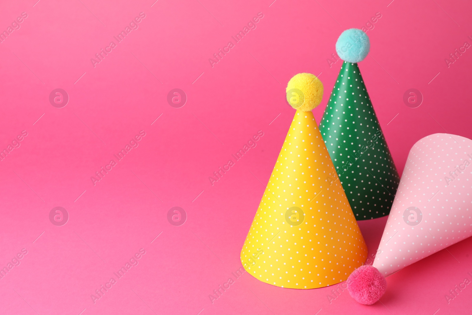 Photo of Beautiful party hats with pompoms on pink background, space for text