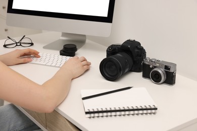 Photo of Photographer working on computer at white table with cameras indoors, closeup