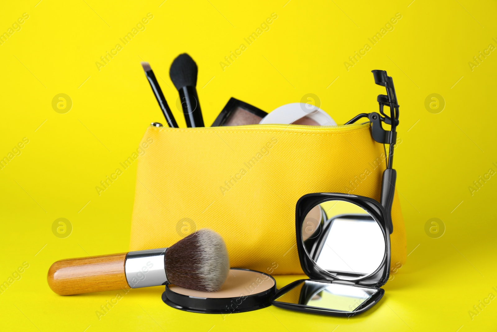 Photo of Stylish pocket mirror and cosmetic bag with makeup products on yellow background
