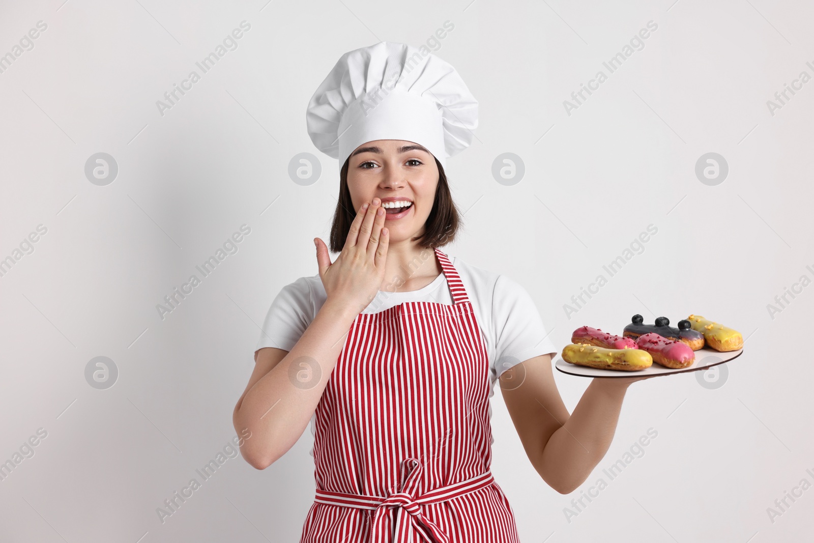 Photo of Happy confectioner with delicious eclairs on light grey background