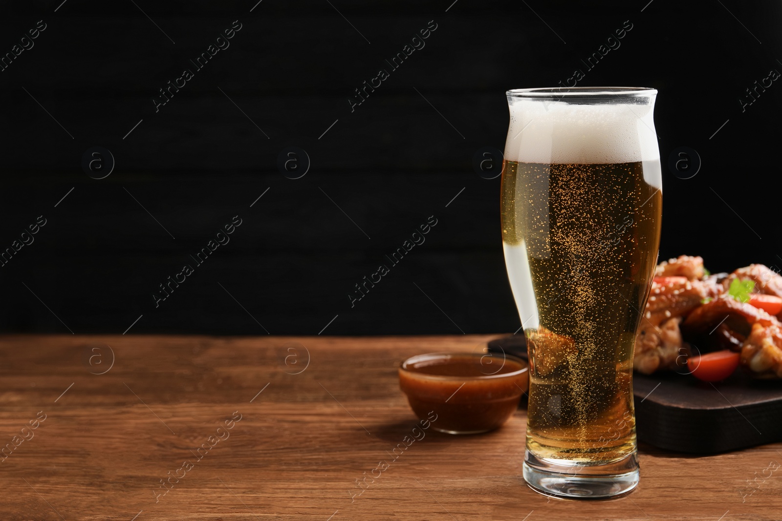 Photo of Glass of beer, delicious baked chicken wings and sauce on wooden table. Space for text