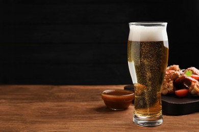 Glass of beer, delicious baked chicken wings and sauce on wooden table. Space for text